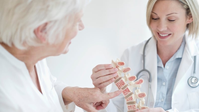 Donna anziana sorride mentre utilizza un dispositivo di magnetoterapia a casa per trattare l’osteoporosi, seduta comodamente su un divano con luce naturale.